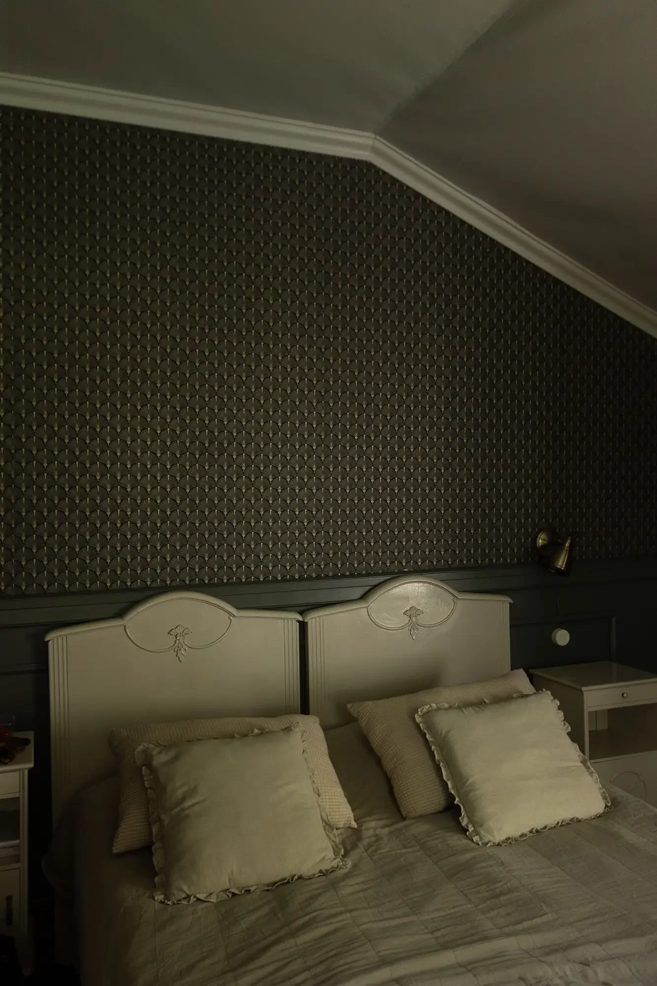 Schlafzimmer unter der Dachschräge mit gemusterter Tapete und zwei bemalten Kopfteilen